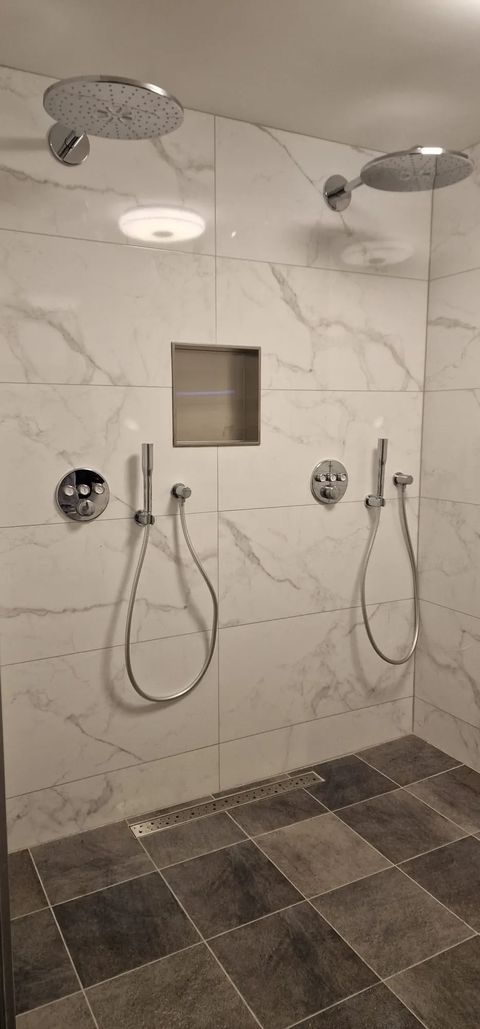 Double douche à l’italienne en marbre blanc avec deux douches de tête et niche de rangement