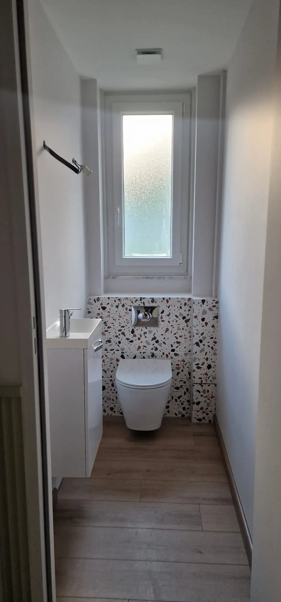 WC suspendu avec mur en carrelage terrazzo coloré, meuble lave-mains et sol effet parquet